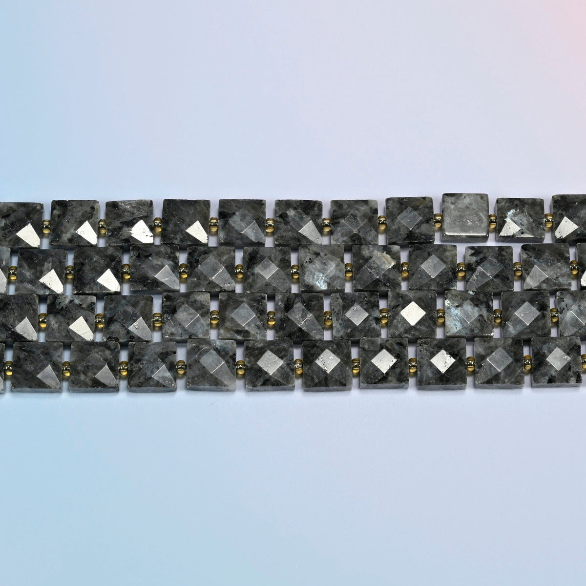 Several strands of natural black labradorite faceted flat square beads laid in straight rows