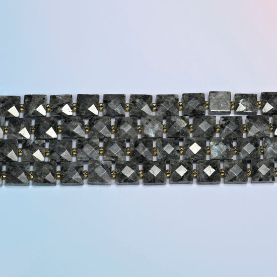 Several strands of natural black labradorite faceted flat square beads laid in straight rows