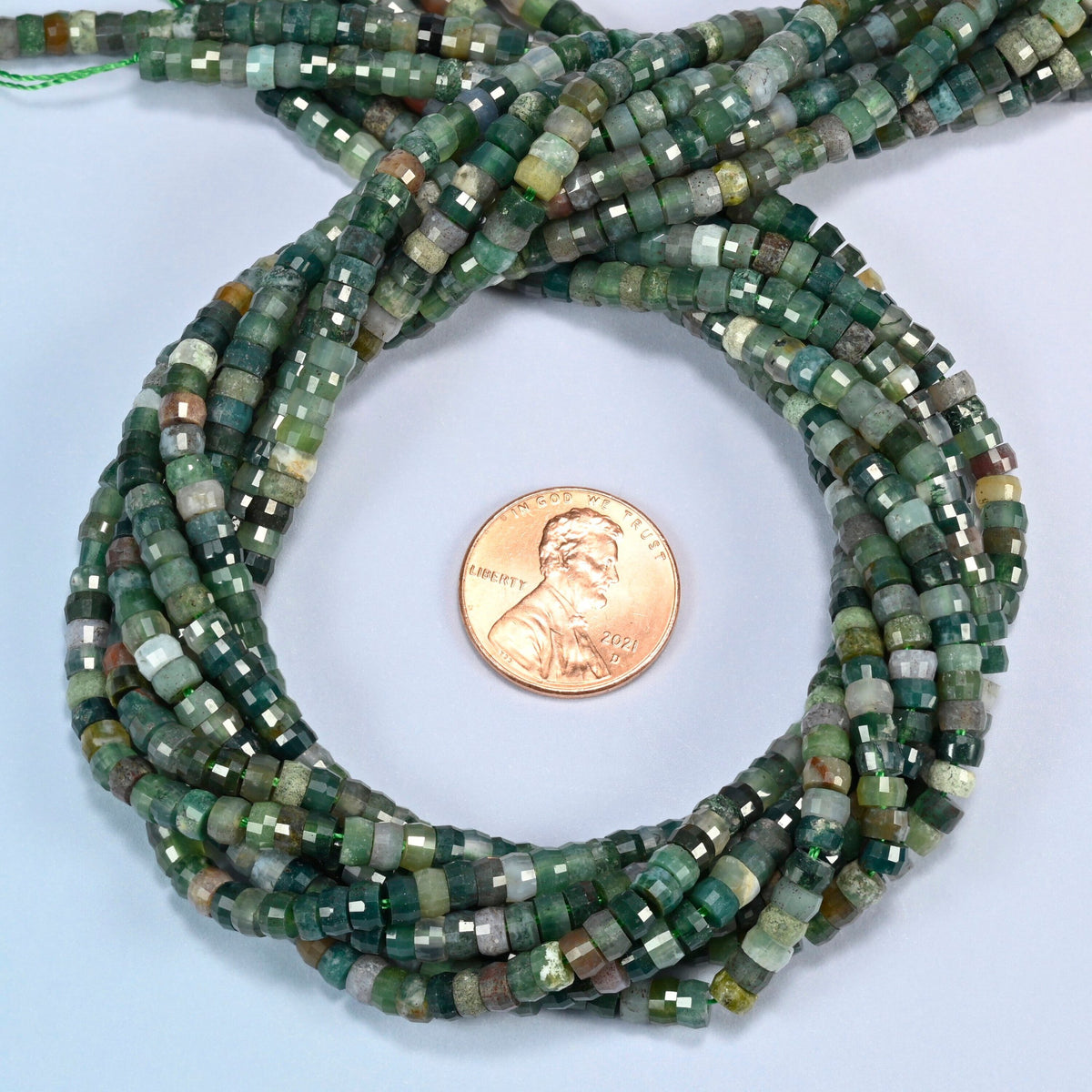 Indian agate faceted heishi disc beads 2x4mm coiled in a loop around a US penny for scale, close-up of the faceted disc shape