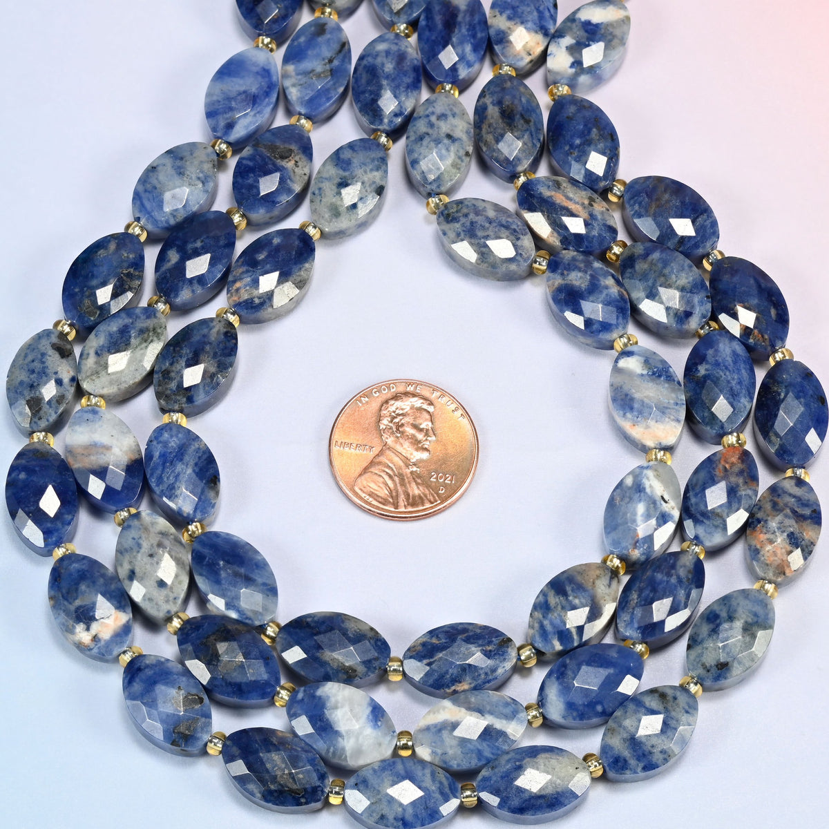 Orange sodalite faceted flat oval strands formed into a teardrop loop around a US penny for scale