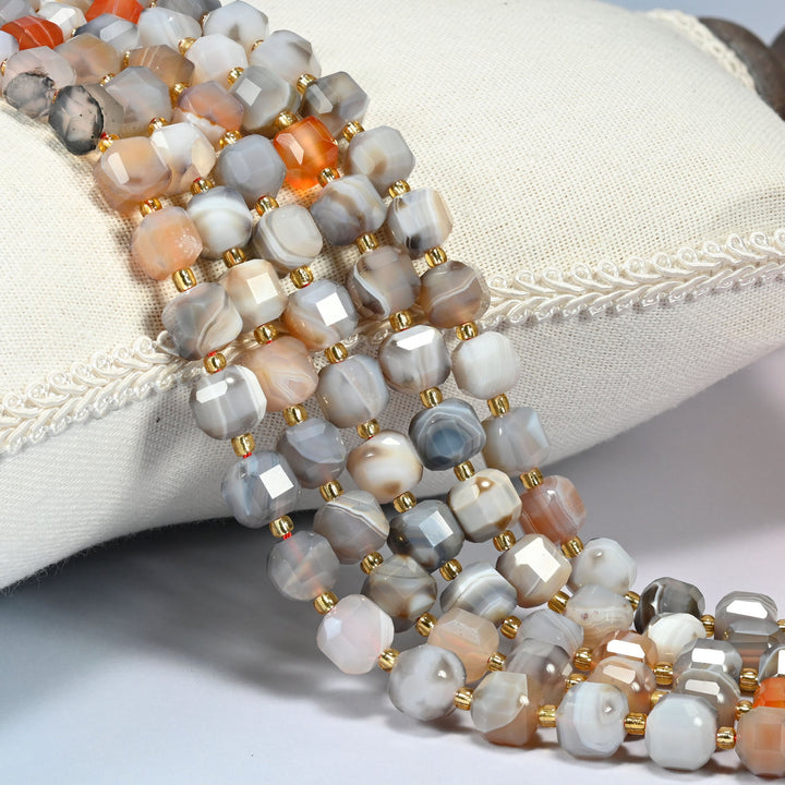 Botswana agate faceted cube beads 6mm and 8mm with small gold spacer beads, several strands draped over a white cushion