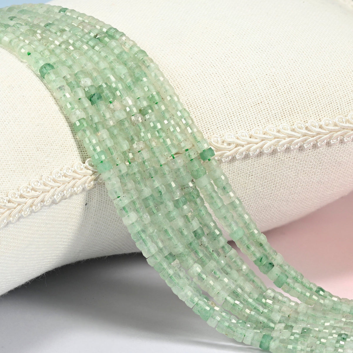Green strawberry quartz faceted heishi disc beads 2x4mm, several strands draped over a white cushion