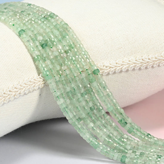 Green strawberry quartz faceted heishi disc beads 2x4mm, several strands draped over a white cushion
