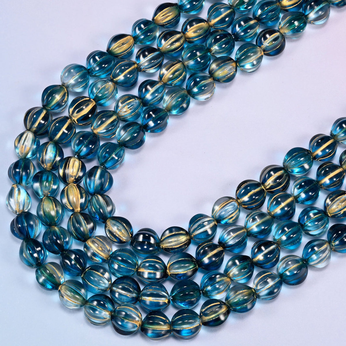 Dark blue gold pumpkin glass beads, several strands laid in a wide sweeping curve across the frame.