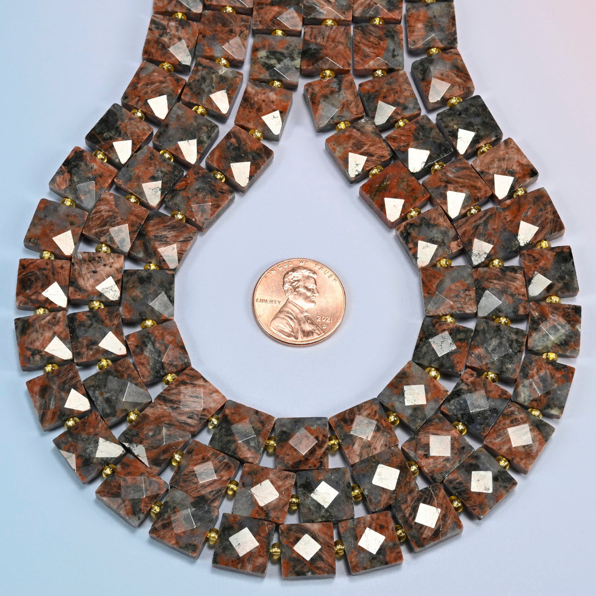 Natural red sesame jasper faceted flat square strands formed into a teardrop loop around a US penny for scale