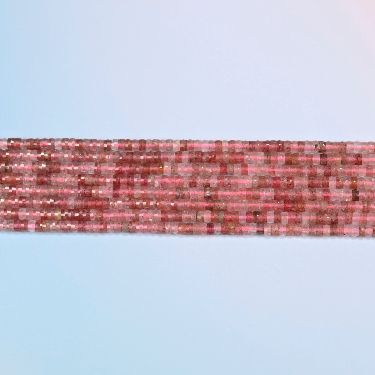 Several strands of strawberry quartz faceted heishi disc beads laid in straight rows
