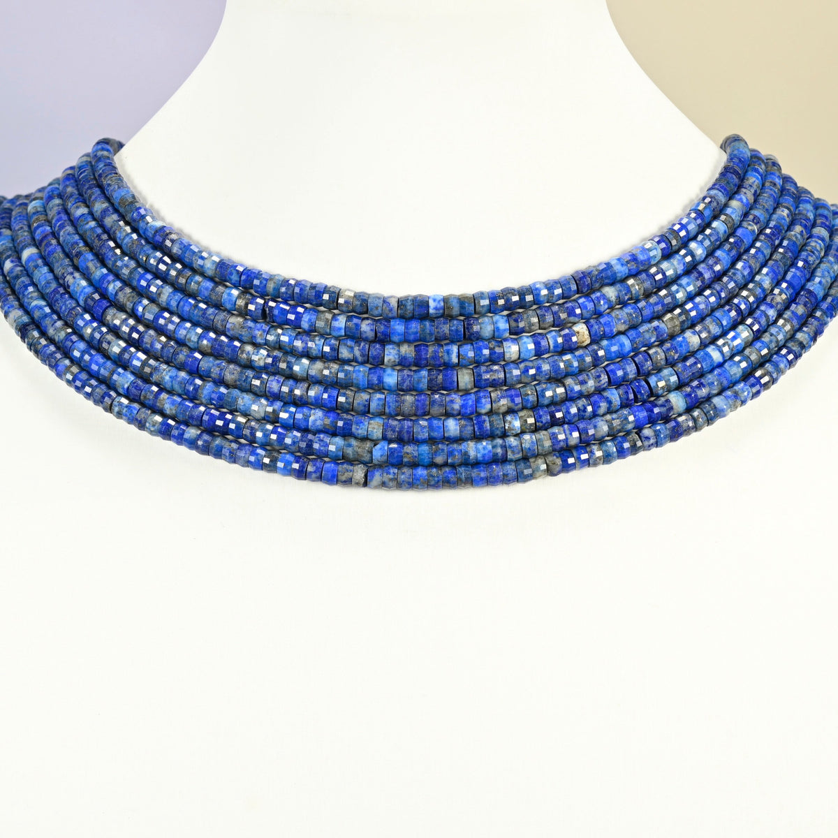 Lapis faceted heishi disc strands arranged as a layered collar on a white display bust, blue beads across the neck