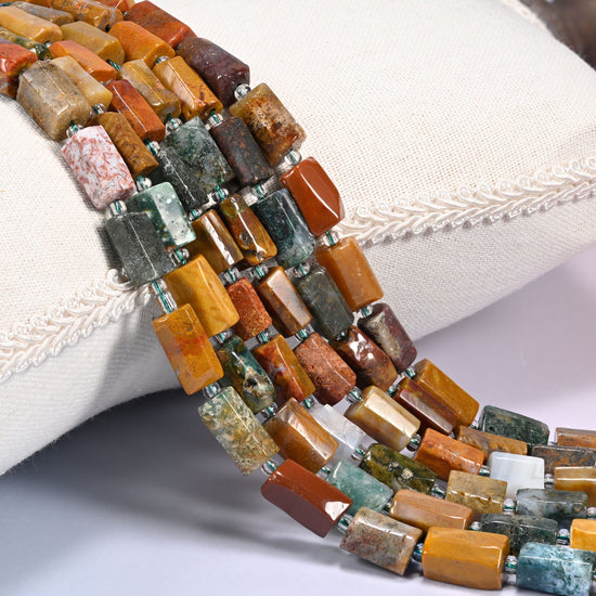 Close-up of multiple strands of faceted Ocean Jasper tube beads with clear glass spacer beads, draped over a cream fabric jewelry display bust.