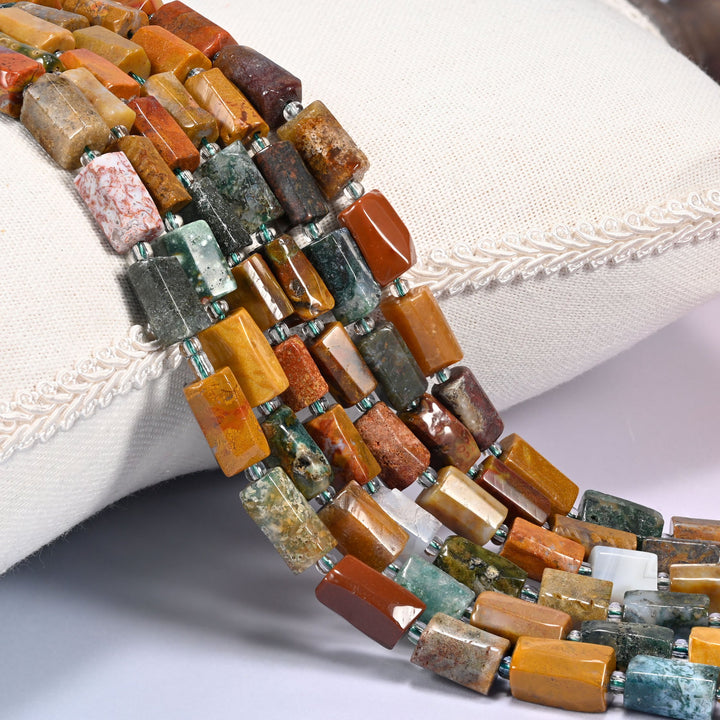Close-up of multiple strands of faceted Ocean Jasper tube beads with clear glass spacer beads, draped over a cream fabric jewelry display bust.