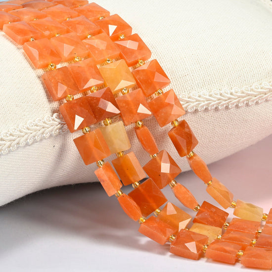 Natural red aventurine faceted flat square beads 10x10mm with small gold seed bead spacers, several strands draped over a white cushion