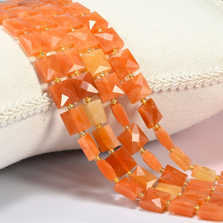 Natural red aventurine faceted flat square beads 10x10mm with small gold seed bead spacers, several strands draped over a white cushion