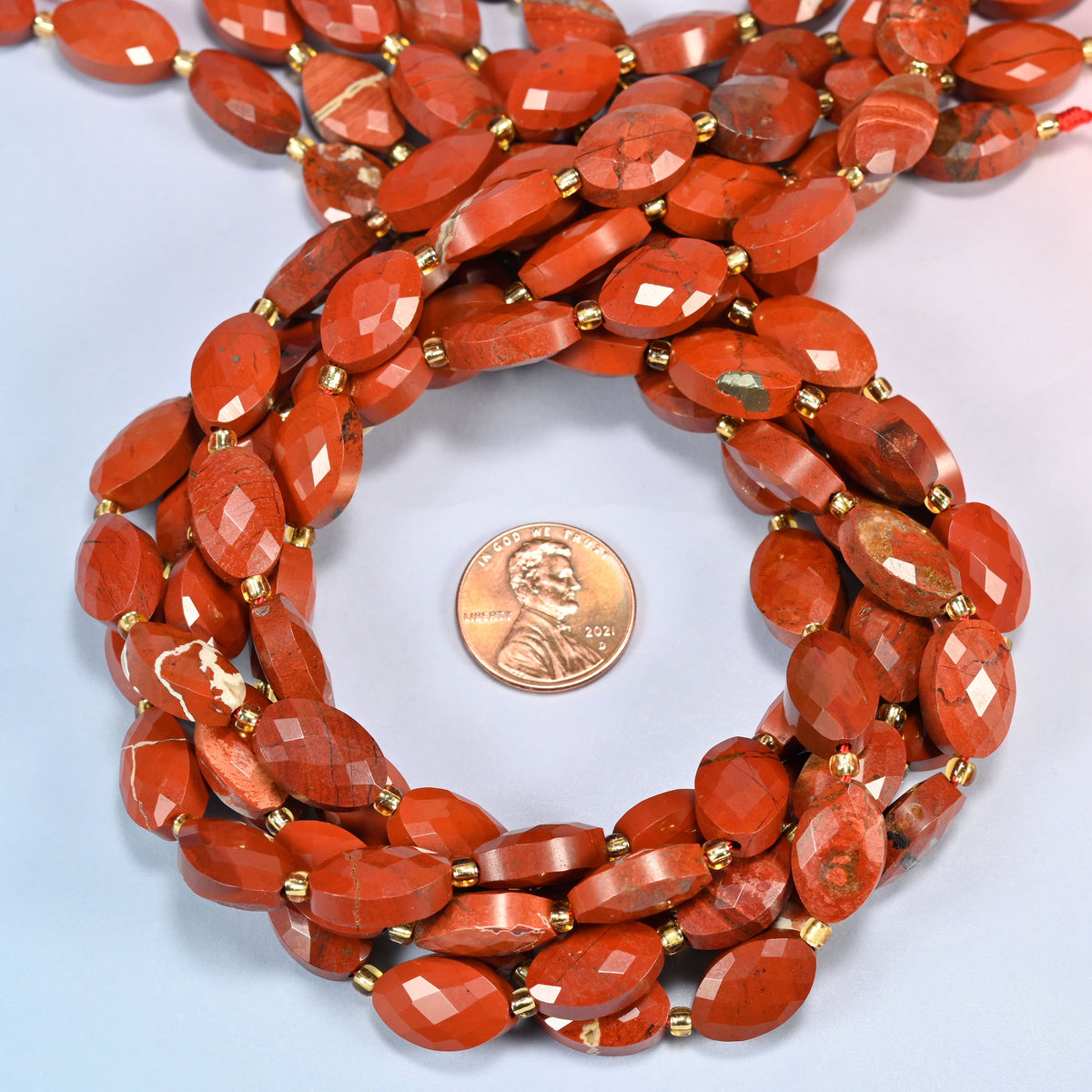 Flower red jasper faceted flat oval beads 9x14mm coiled in a loop around a US penny for scale, close-up of the faceted flat oval shape