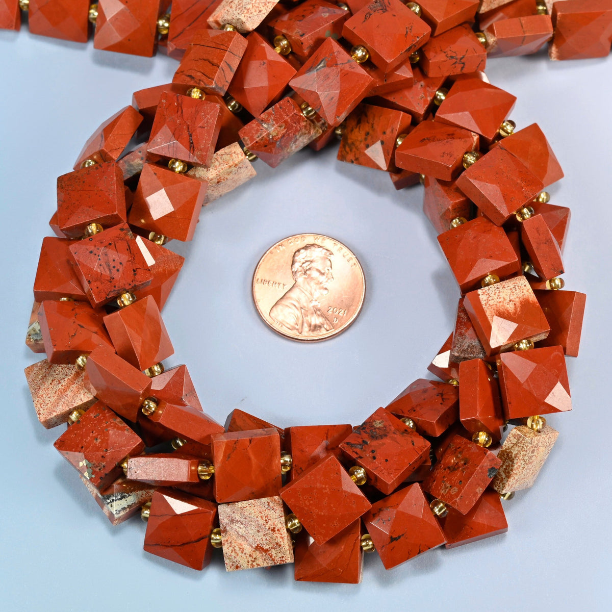 Natural flower red jasper faceted flat square beads 10x10mm coiled in a loop around a US penny for scale, close-up of the faceted flat square shape
