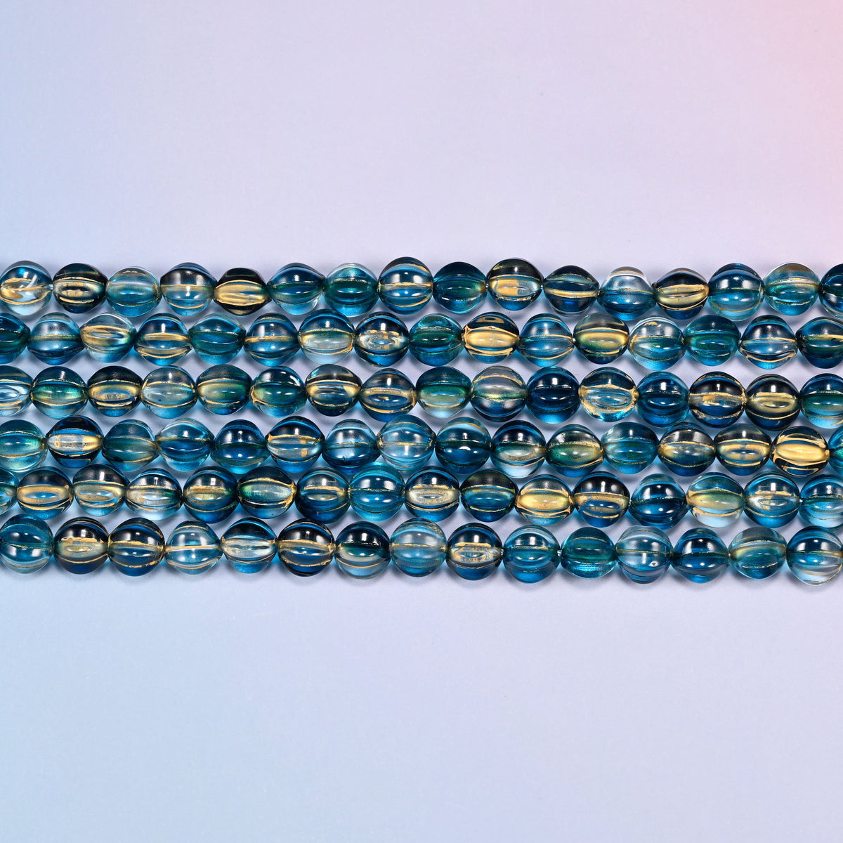 Close-up of 8mm dark blue gold pumpkin glass beads in four horizontal rows, showing the carved melon ribs.