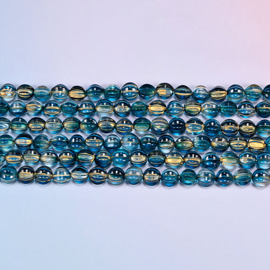 Close-up of 8mm dark blue gold pumpkin glass beads in four horizontal rows, showing the carved melon ribs.