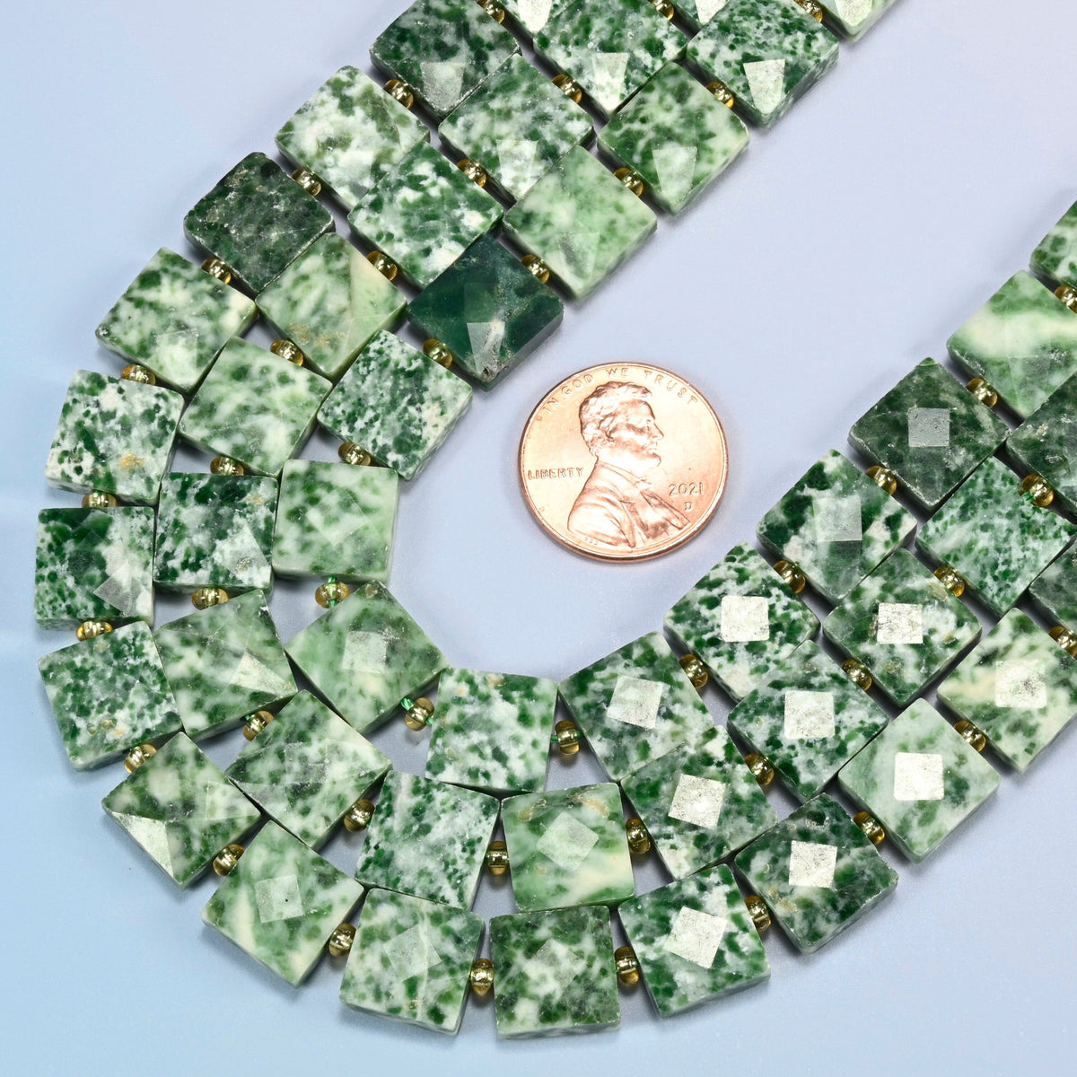 Close view of tree agate faceted flat square strands curving beside a US penny for scale