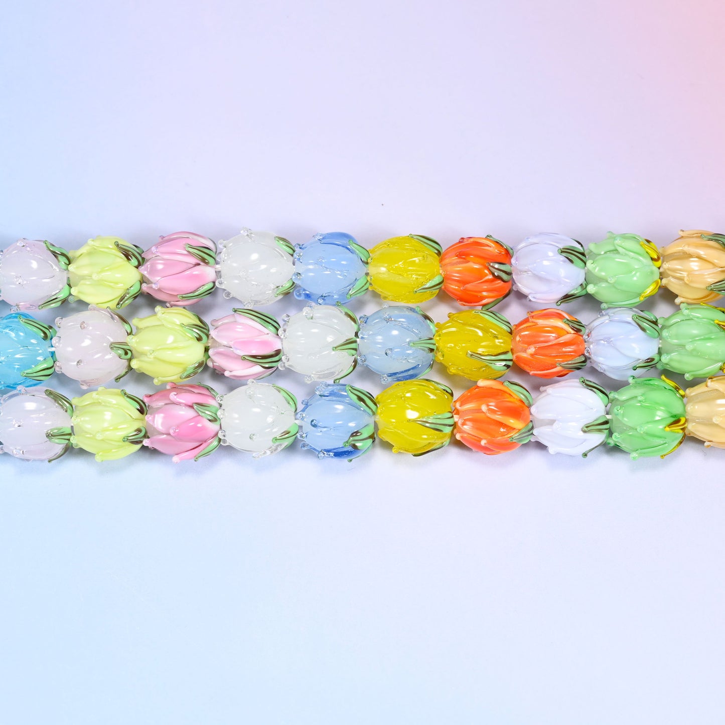 Close-up rows of pastel tulip bud lampwork glass beads in blue, white, yellow, and pink tones, laid in a dense repeating pattern.