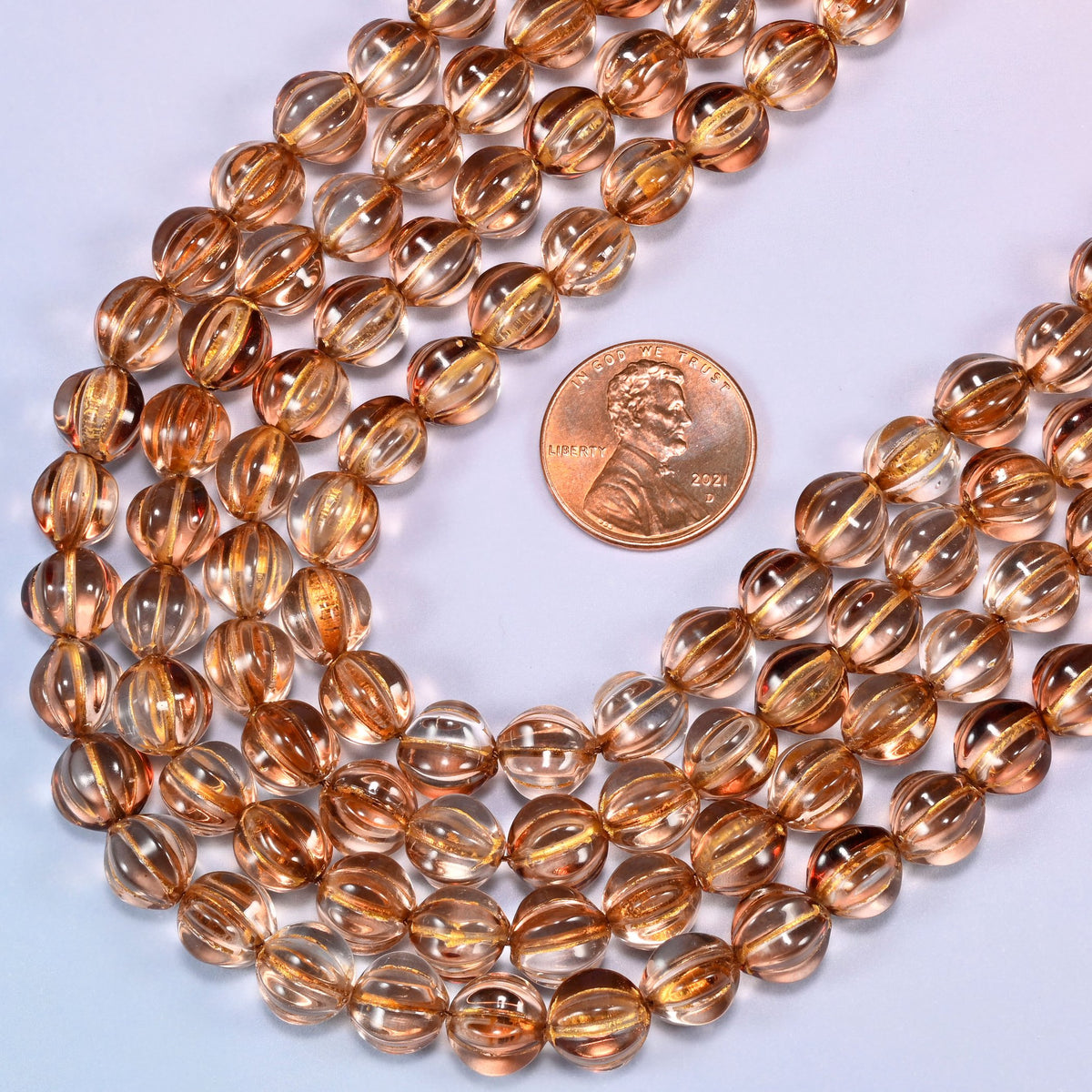 Brown pumpkin glass beads coiled loosely, shown with a US penny resting on the strands for scale.