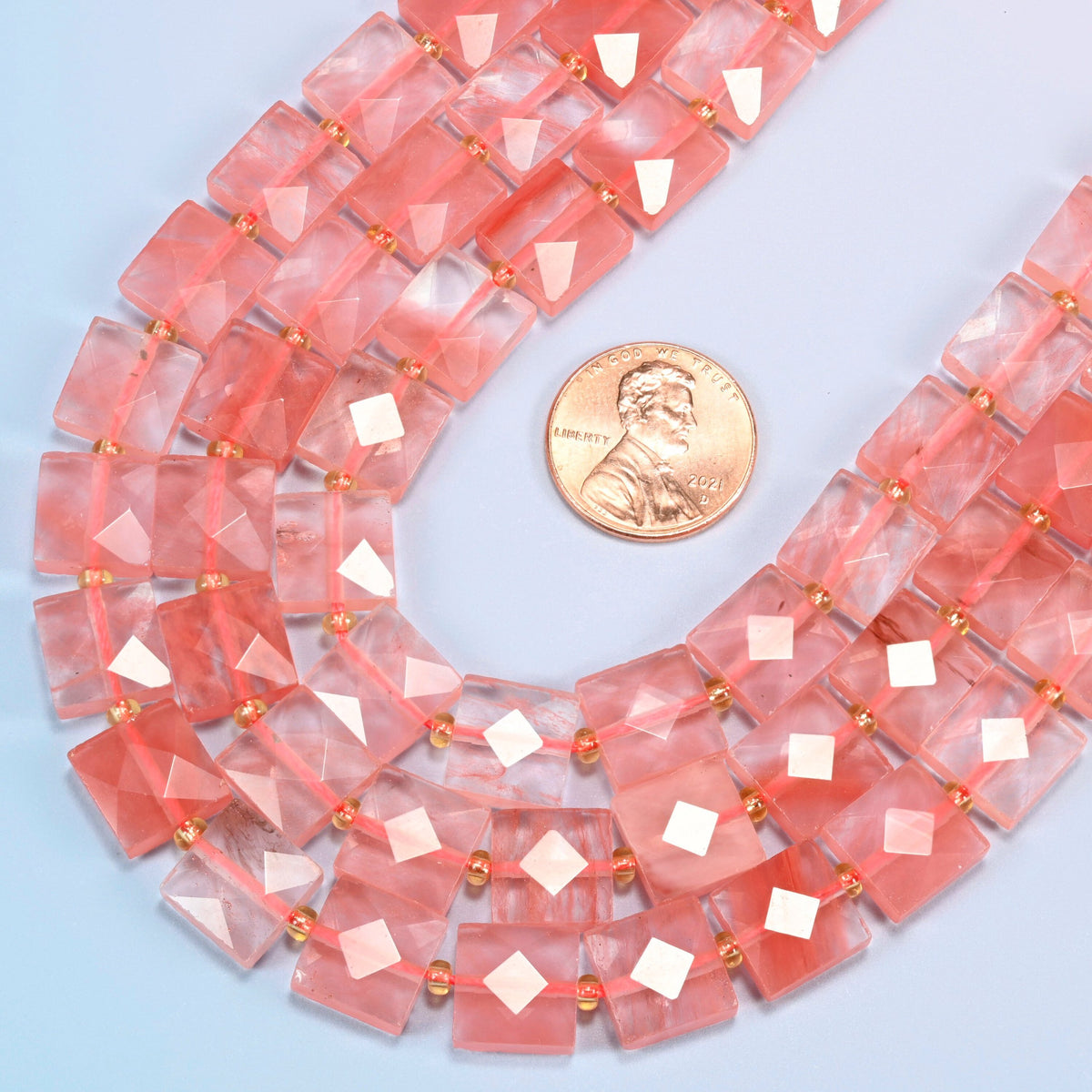 Close view of melon quartz faceted flat square strands curving beside a US penny for scale