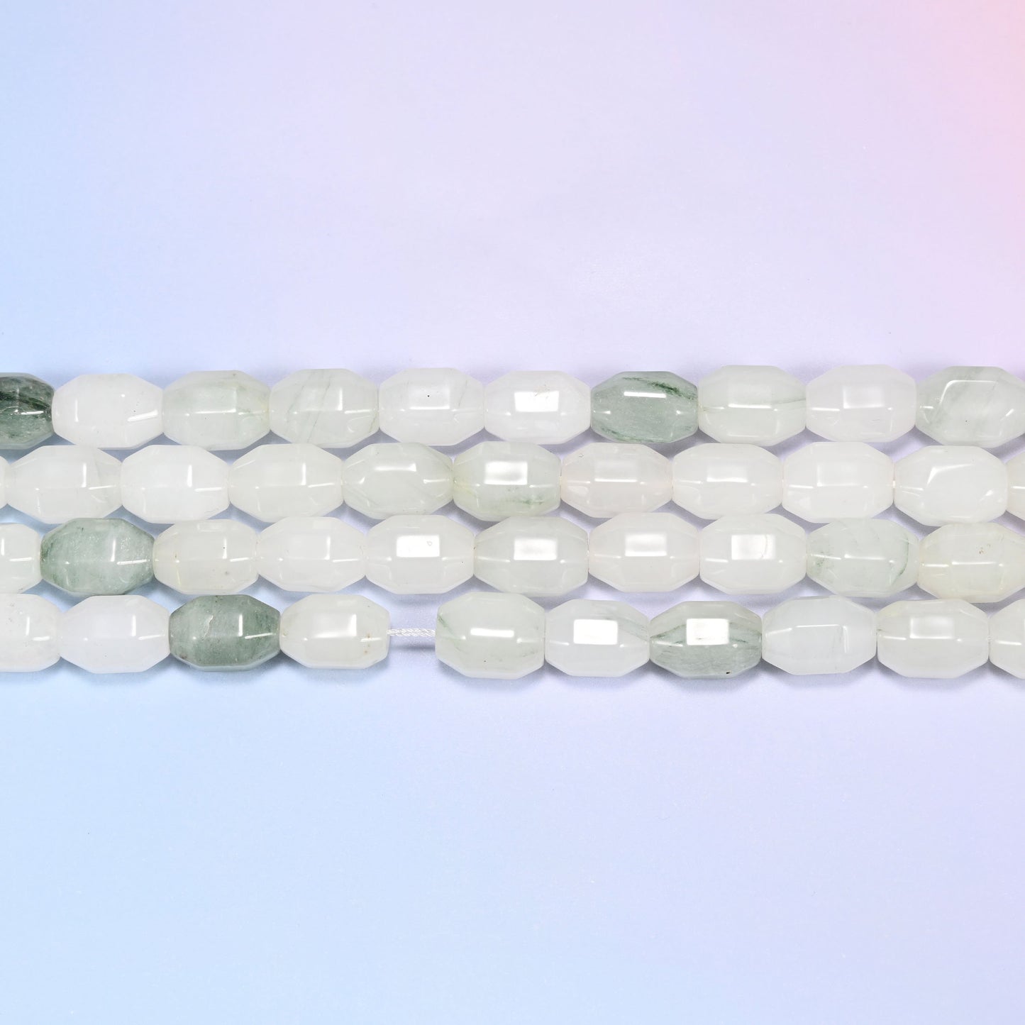 Close-up rows of Tianshan Jade faceted barrel beads laid flat, showing the mostly white and cream tone with sage green marbled beads mixed in.