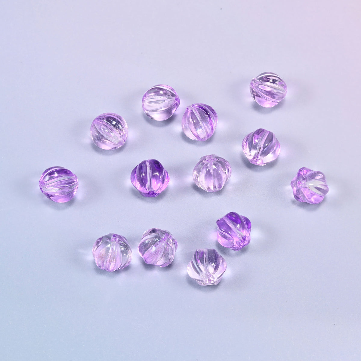 A scattered group of loose 8mm clear purple pumpkin glass beads, showing the melon ribs and the drill holes.