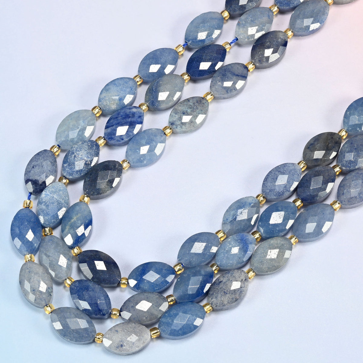 Blue aventurine faceted flat oval beads in several strands curved into a wide U, light to dark blue stone