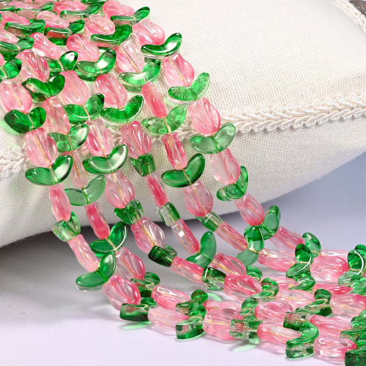 Close-up of pink tulip flower and green leaf glass beads cascading diagonally over a cream woven pillow with decorative trim.