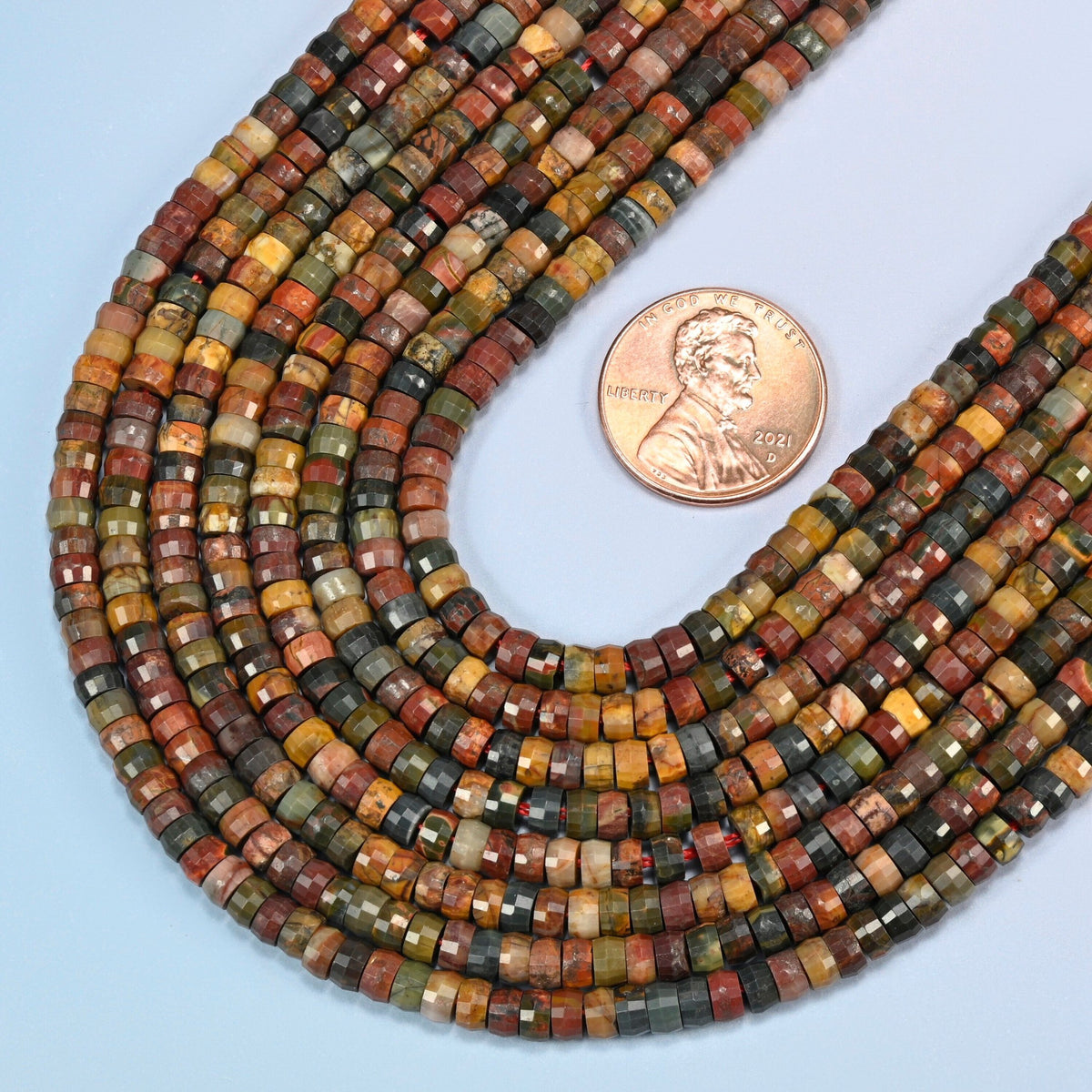Close view of red howlite faceted heishi disc strands curving beside a US penny for scale