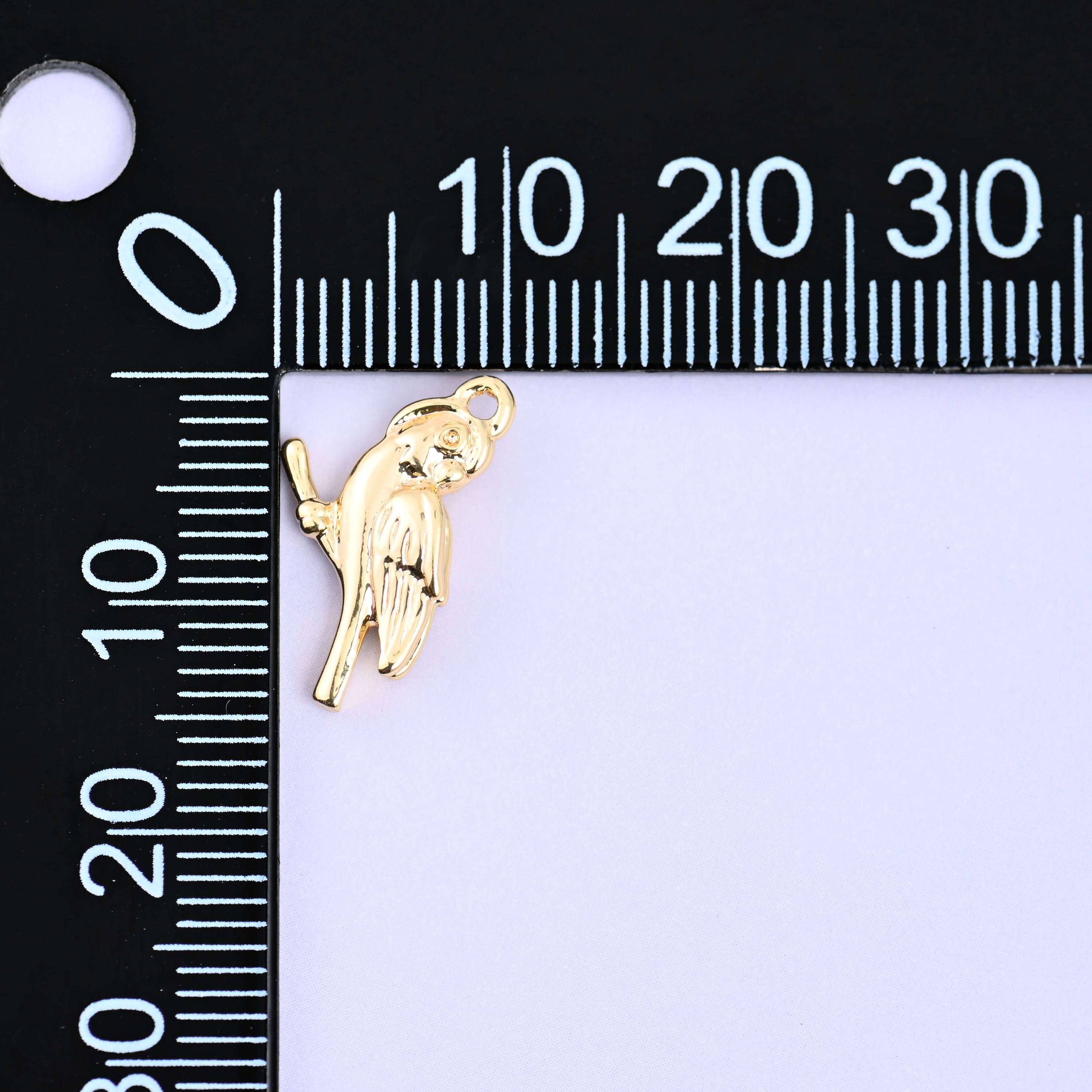 Small gold charms bird measured against a millimeter ruler showing the 15.9mm length