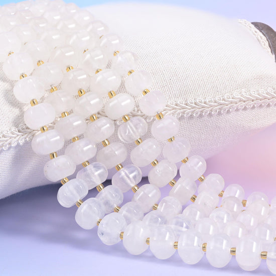 Clear quartz pumpkin rondelle strands on a white cushion, frosted white beads split by gold seed spacers