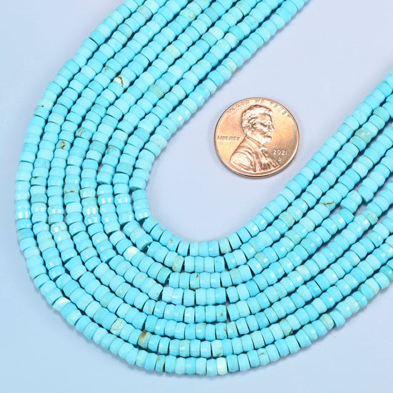 Close view of dyed blue howlite faceted heishi disc strands curving beside a US penny for scale
