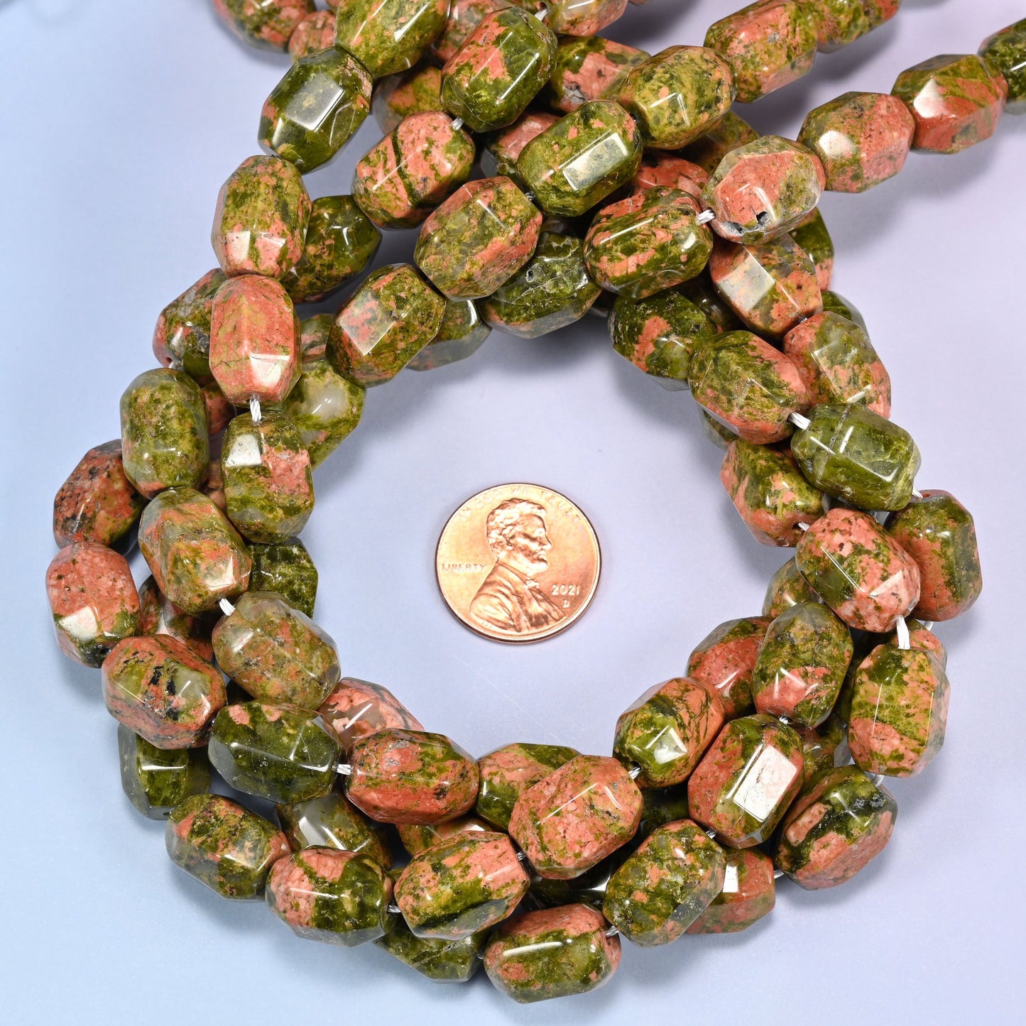 Wide circular coil of faceted Unakite barrel beads on a light blue background, showing the full wreath pattern.