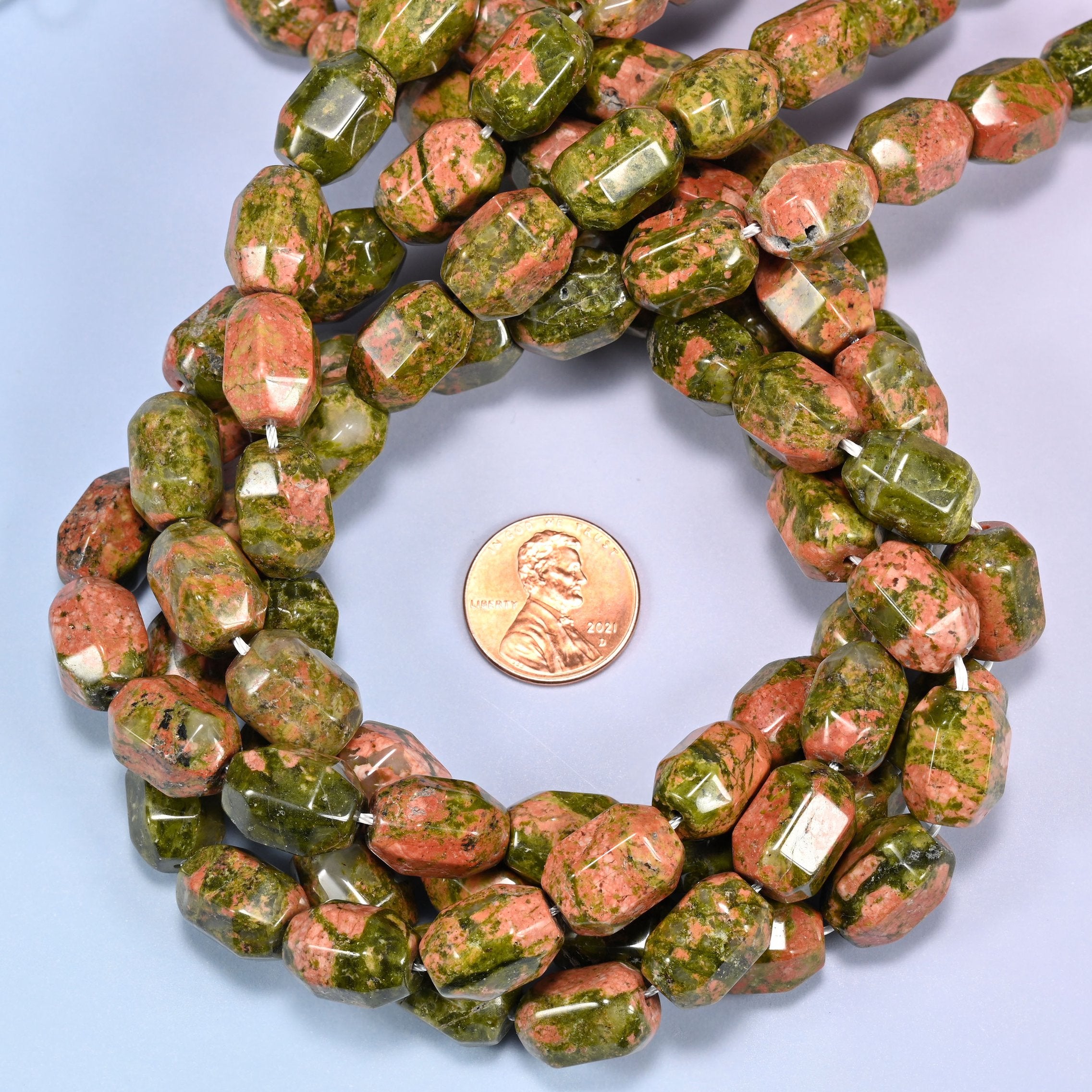 Wide circular coil of faceted Unakite barrel beads on a light blue background, showing the full wreath pattern.