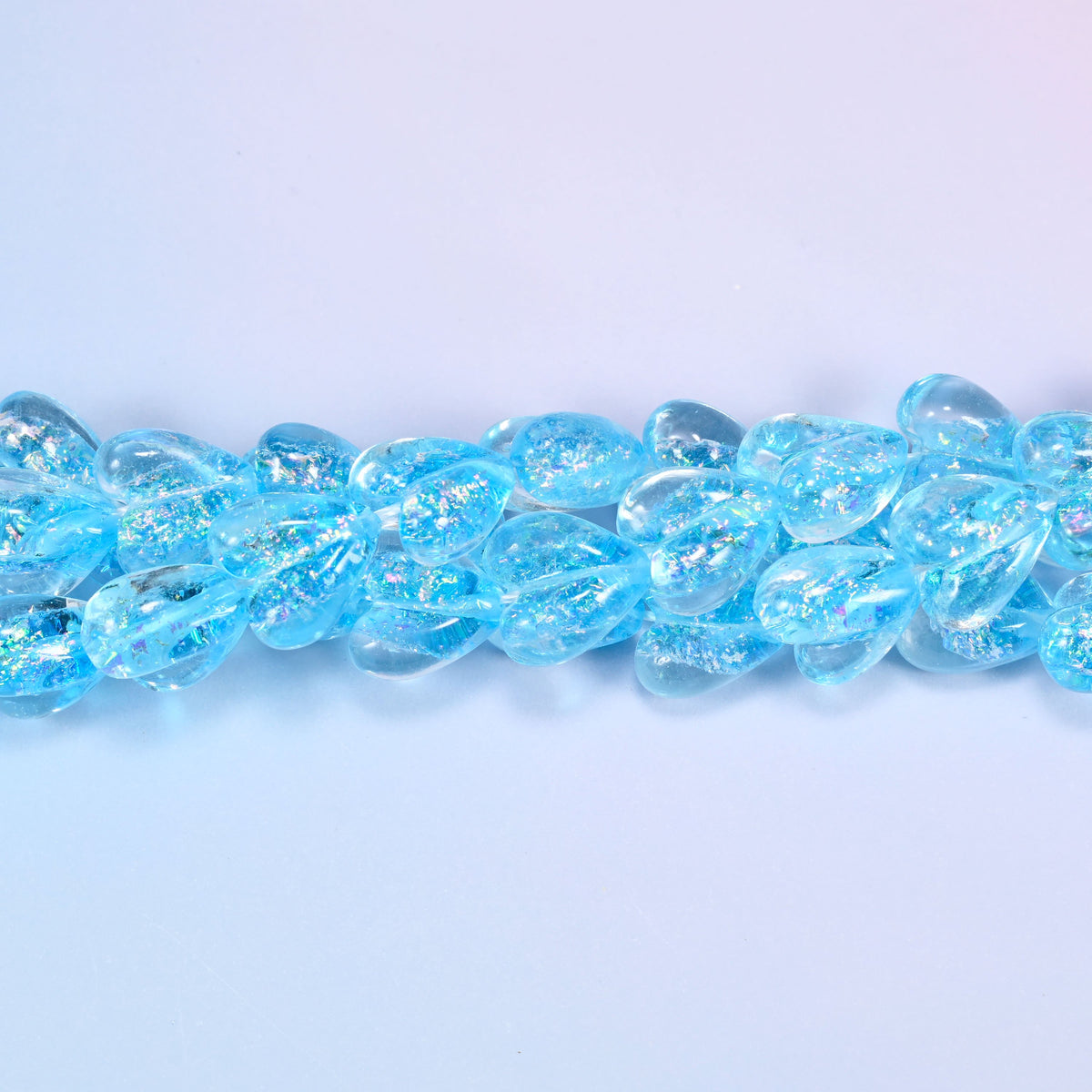 Iridescent light blue heart glass beads in a close straight row, showing the even moulded heart shape