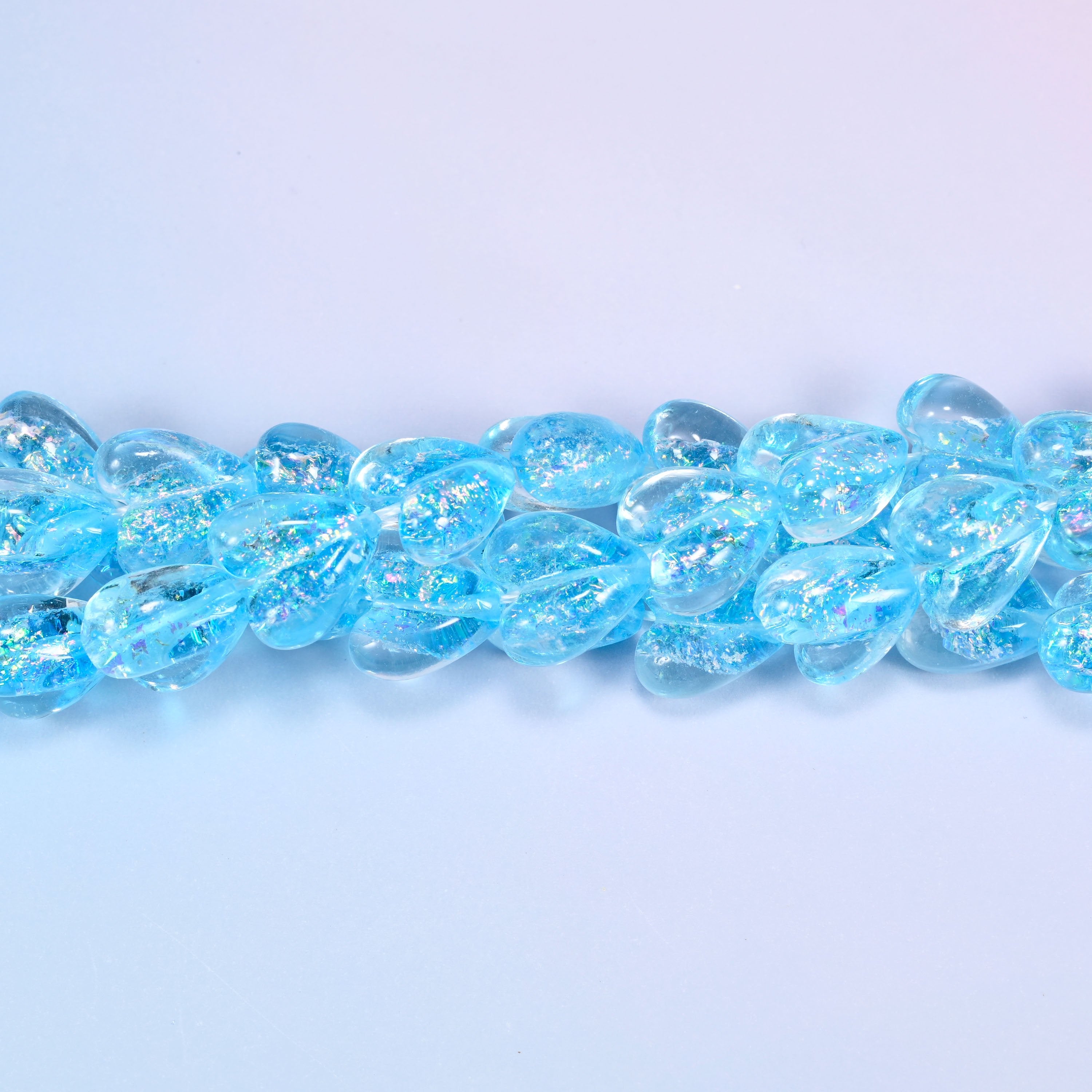 Iridescent light blue heart glass beads in a close straight row, showing the even moulded heart shape