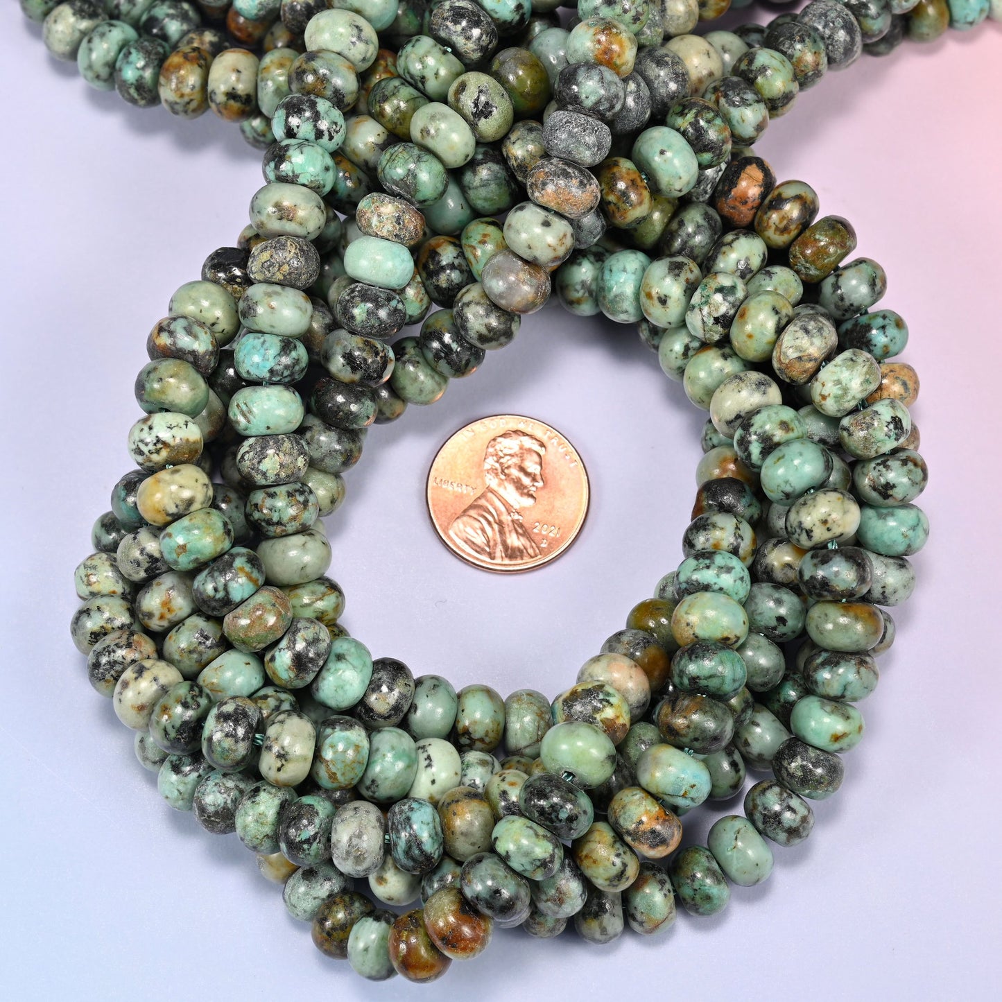Multiple strands of African Howlite beads gathered together on a lavender surface, loose ends visible.