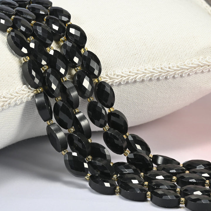 Black onyx faceted flat oval beads 9x14mm with small gold seed bead spacers, several strands draped over a white cushion