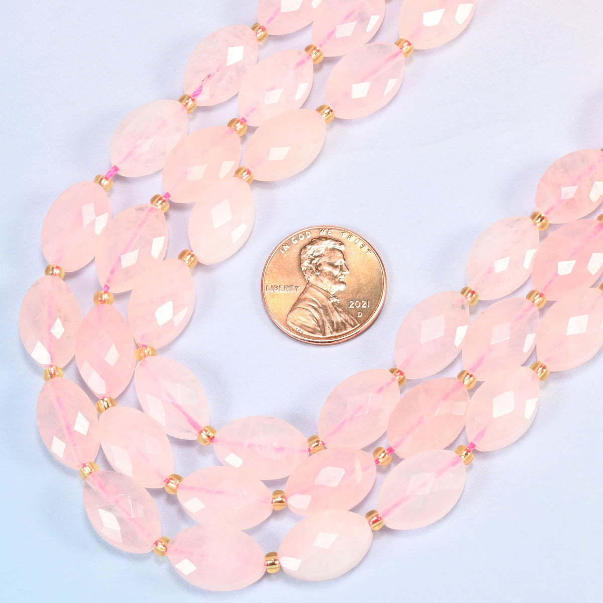 Close view of rose quartz faceted flat oval strands curving beside a US penny for scale