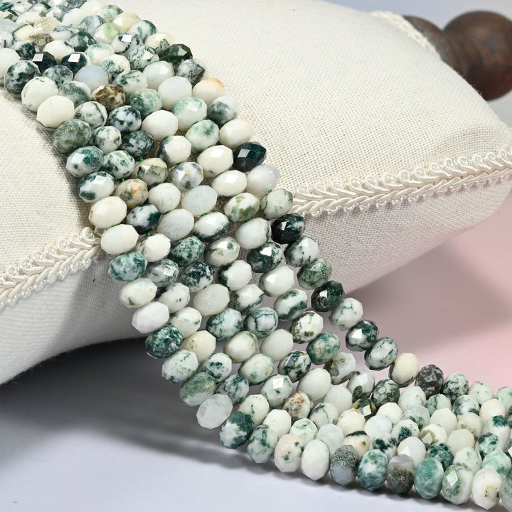 Tree agate faceted rondelle beads 5x8mm in creamy white with forest green veining, several strands draped over a white cushion