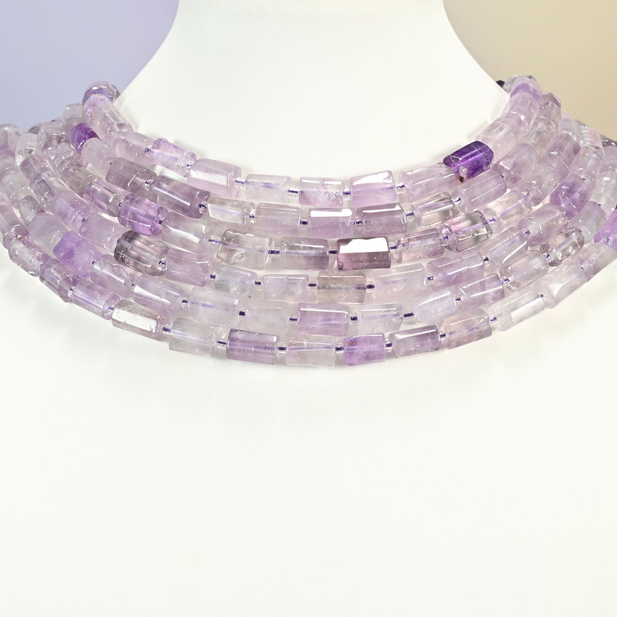 Lavender amethyst faceted tube beads layered as graduated collar rows on a white neck display bust, soft lilac and near-clear.