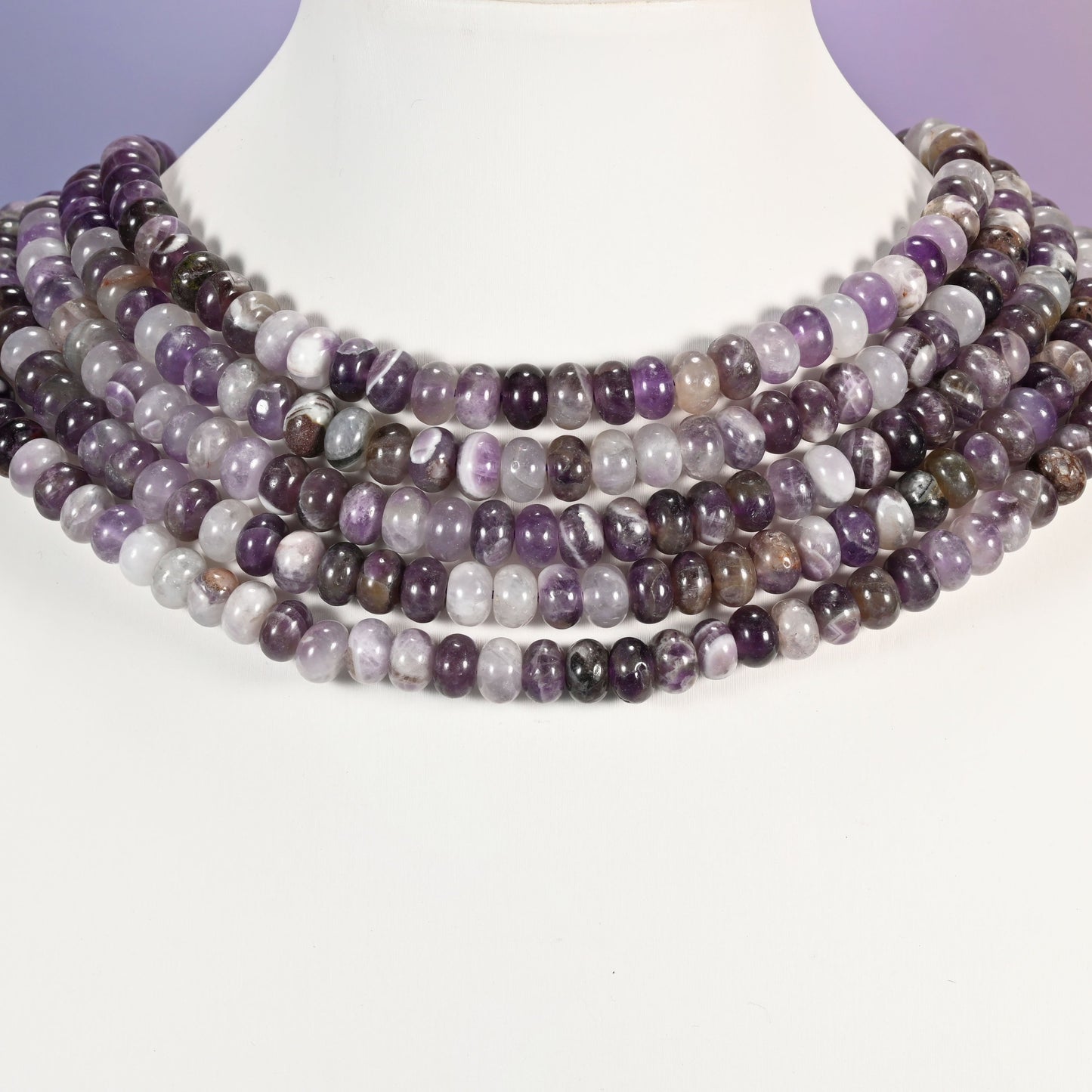 Multi-strand Amethyst necklace laid flat on a mannequin neck form against a lavender background.
