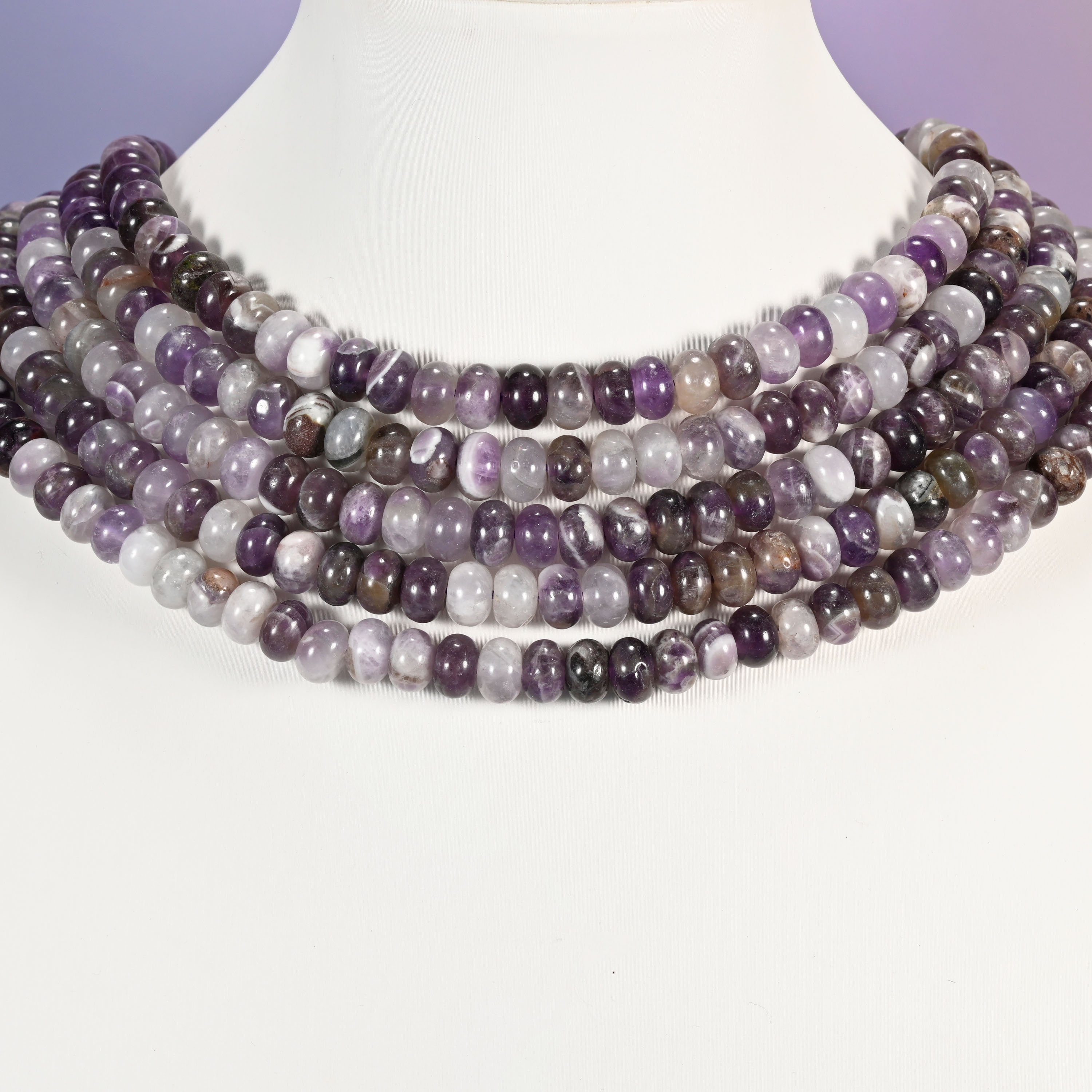 Multi-strand Amethyst necklace laid flat on a mannequin neck form against a lavender background.