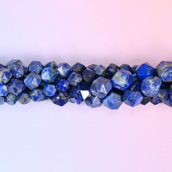 Blue Lapis Lazuli faceted beads close up in a single row, flat triangular star cut planes with small gold pyrite flecks