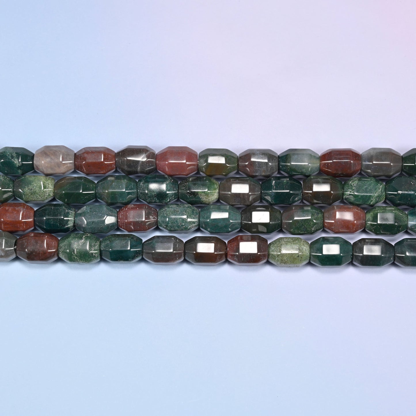 Close-up rows of Indian Agate faceted barrel beads laid horizontally flat, showing the deep green, olive, rust, and gray color mix.