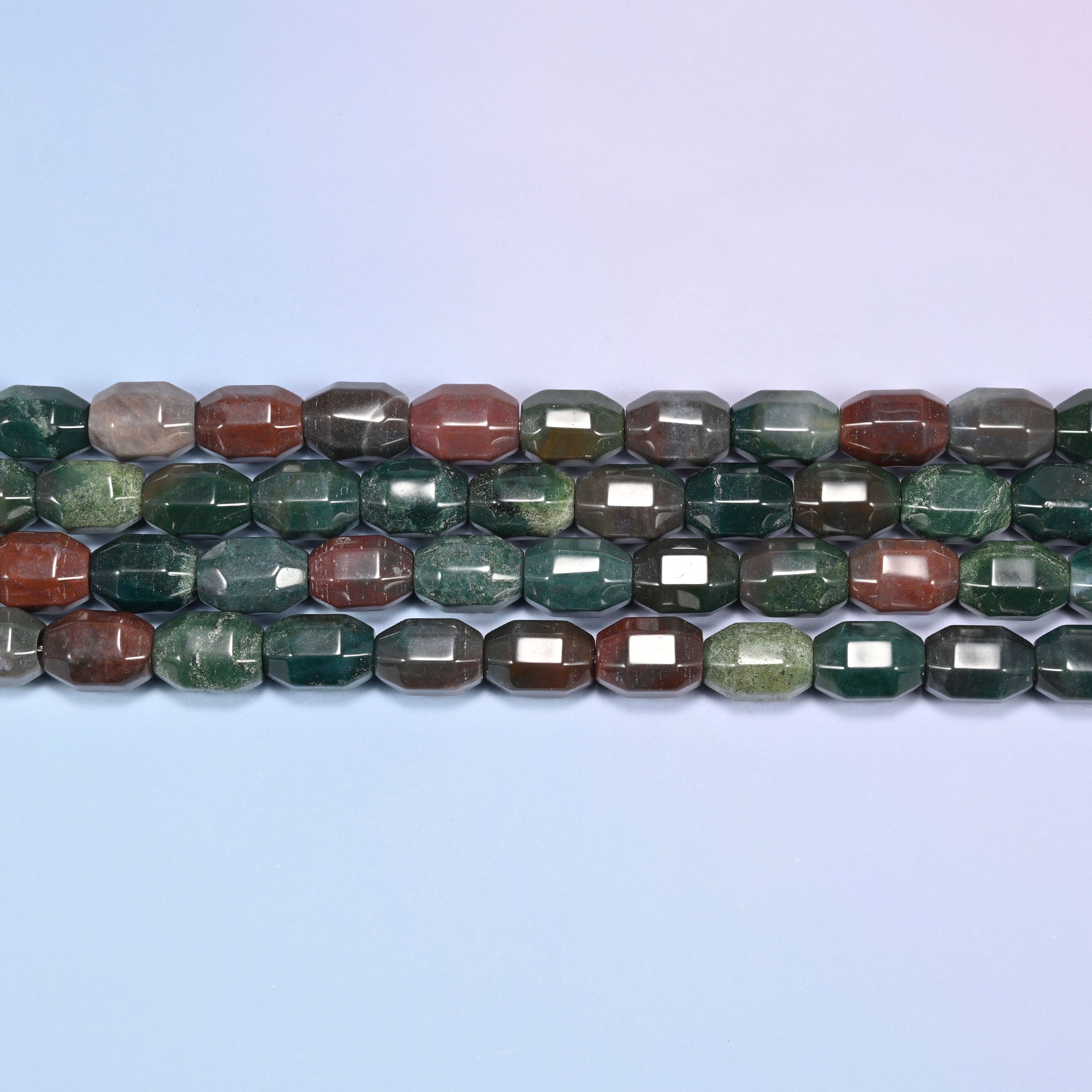 Close-up rows of Indian Agate faceted barrel beads laid horizontally flat, showing the deep green, olive, rust, and gray color mix.