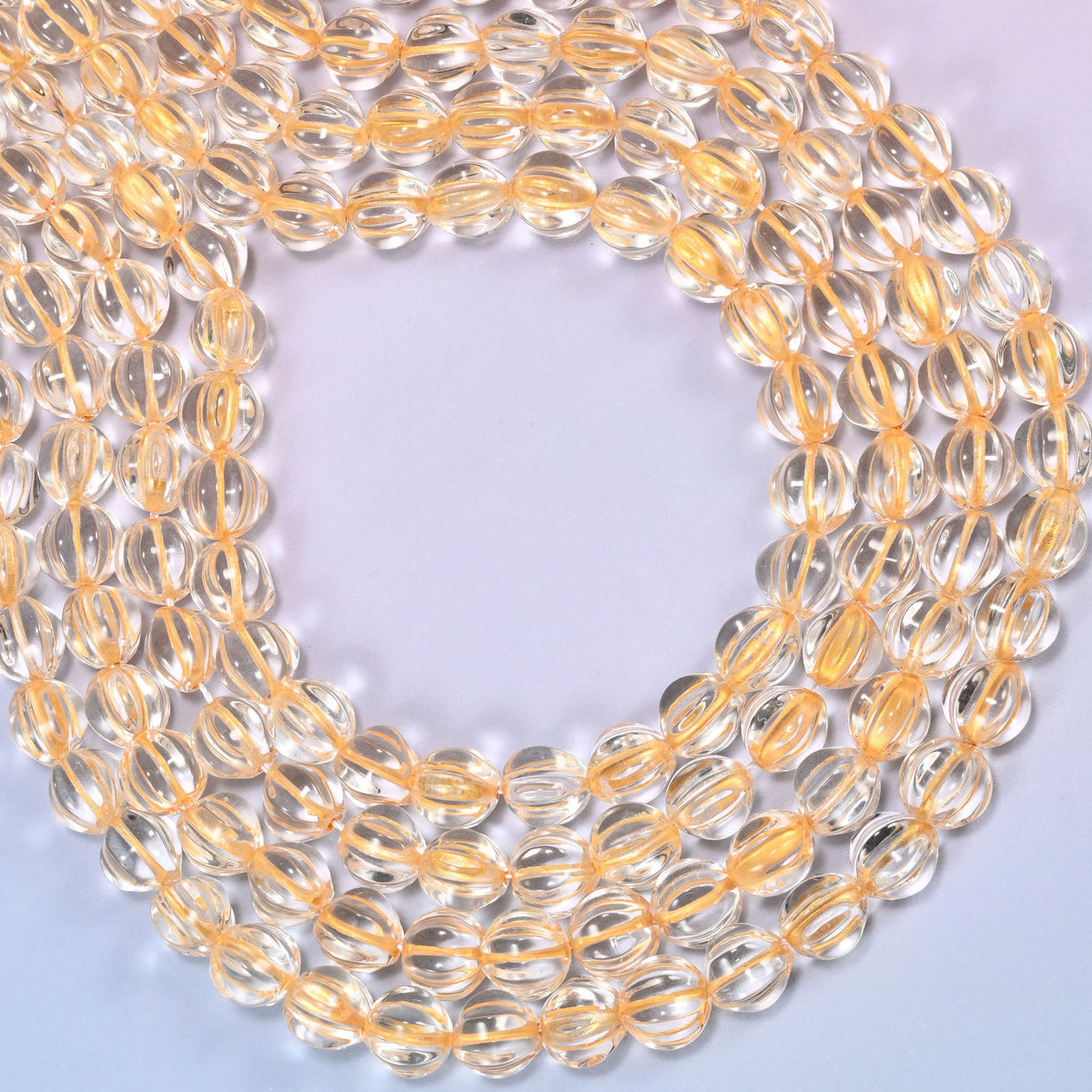 Clear gold pumpkin glass beads coiled loosely, shown with a US penny resting on the strands for scale.