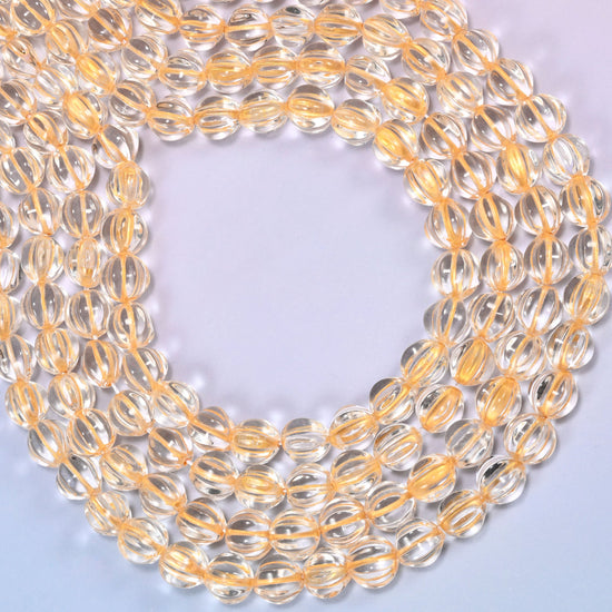 Clear gold pumpkin glass beads coiled loosely, shown with a US penny resting on the strands for scale.