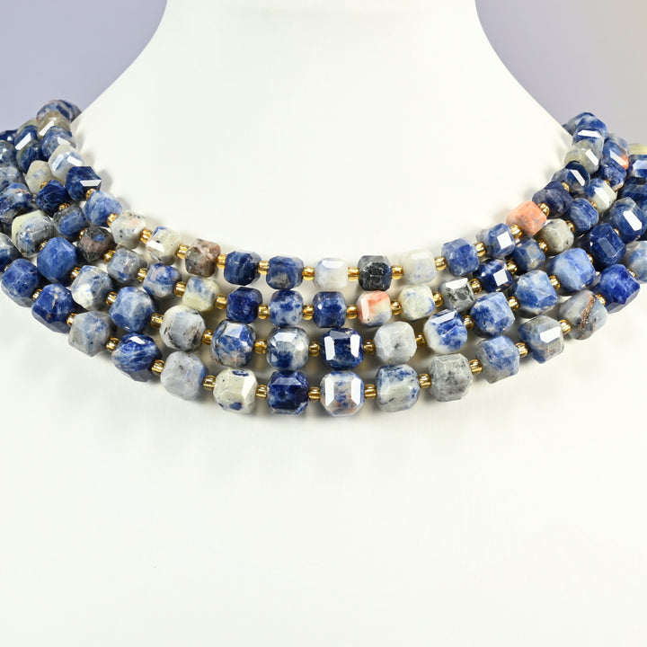 Orange sodalite faceted cube strands arranged as a layered collar on a white display bust, deep blue, white and peach beads across the neck