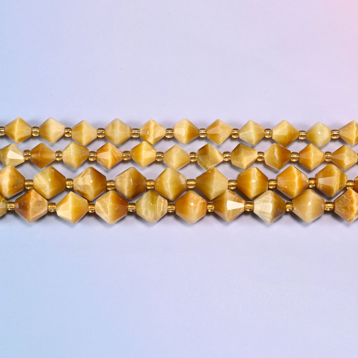 Gold tiger eye bicone beads in straight rows, seen close up, each bead cut to two points meeting at a wide center.