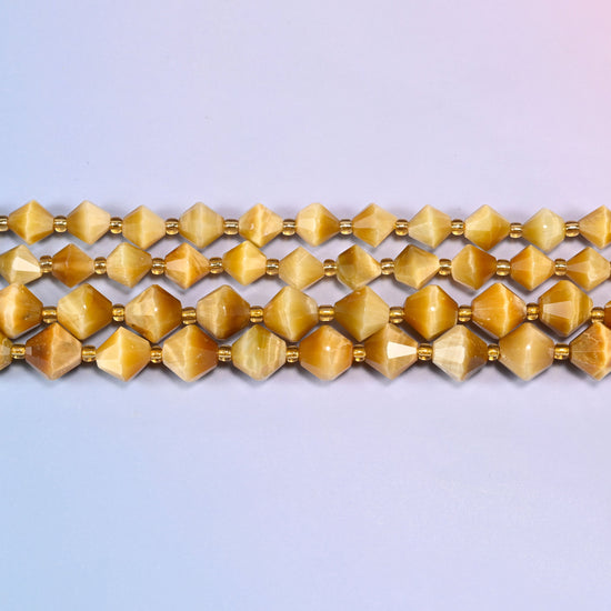 Gold tiger eye bicone beads in straight rows, seen close up, each bead cut to two points meeting at a wide center.